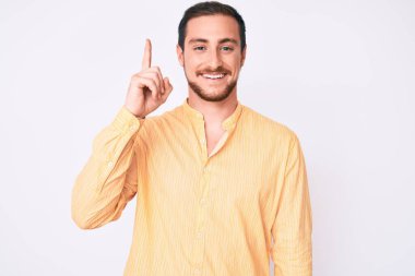 Gündelik giysiler giymiş genç yakışıklı bir adam başarılı bir fikri işaret ediyor. Heyecanlı ve mutlu. Bir numara.. 
