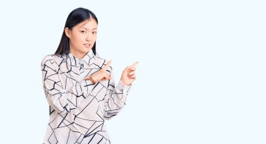 Gündelik tişört giyen genç, güzel Çinli bir kadın iki eliyle endişeli ve gergin bir ifadeye işaret ediyor. 