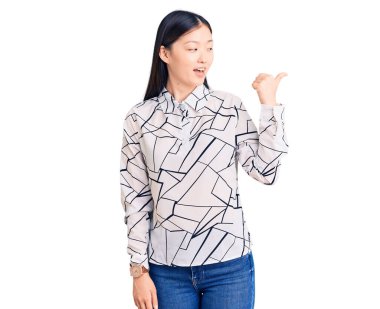 Genç, güzel, Çinli bir kadın, sıradan bir tişört giyiyor, gülümsüyor, gülümsüyor ve başparmağıyla yan tarafa bakıyor.. 