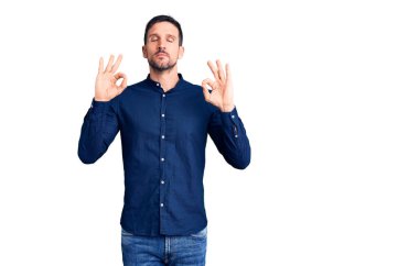 Genç yakışıklı adam rahat gömlekler giyiyor ve gözleri kapalı gülümsüyor parmaklarıyla meditasyon hareketi yapıyor. yoga konsepti. 