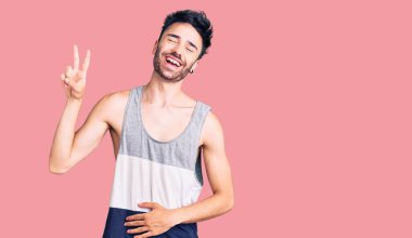 Gündelik kıyafetler giyen, gülümseyen ve kameraya göz kırpan genç İspanyol adam zafer işareti yapıyor. İki numara.. 