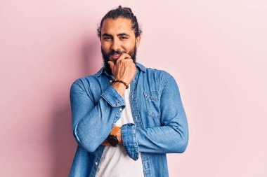 Gündelik giysiler giyen genç Arap adam kameraya kollarını kavuşturup çenesine dokunarak gülümsüyor. Olumlu düşünmek. 