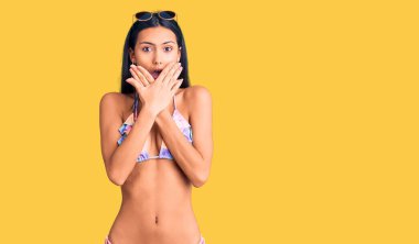 Bikini giyen ve güneş gözlüğü takan genç, güzel bir Latin kız yanlışlıkla ağızlarını kapatarak şok geçirdi. gizli kavram. 