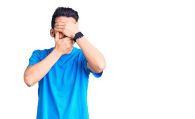 Sakallı, sıradan tişörtlü, gözleri ve ağzı elleri kapalı, şaşırmış ve şok olmuş genç yakışıklı bir adam. duygu gizleme 