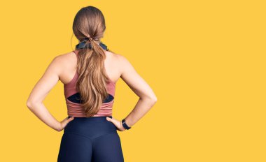 Güzel beyaz kadın spor kıyafetleri giyiyor ve kulaklık takıyor. Arkaya bakıyor. Kolları vücudunda. 