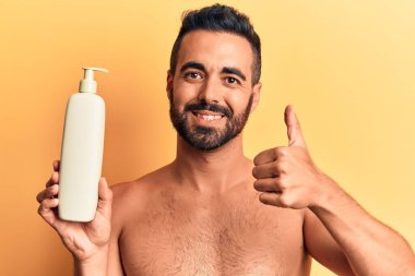 İspanyol asıllı genç adam elinde güneş kremi tutarken gülümsüyor, gülümsüyor ve olumlu bakıyor. 