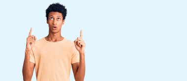 Gündelik giysiler giyen genç Afro-Amerikan adam şaşkın ve şaşırmış bir şekilde yukarı baktı ve parmaklarıyla işaret etti ve kollarını kaldırdı.. 