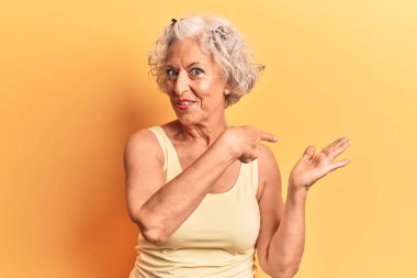 Kıdemli gri saçlı kadın, sıradan kıyafetler giyip kameraya hayret ediyor ve gülümsüyor.. 