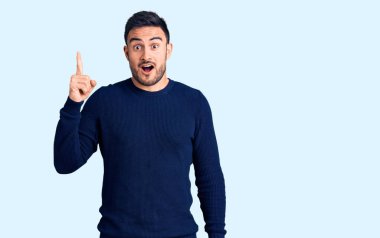 Gündelik giysiler giymiş genç yakışıklı bir adam başarılı bir fikri işaret ediyor. Heyecanlı ve mutlu. Bir numara.. 