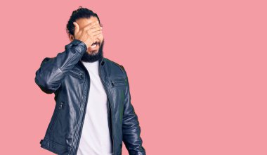 Gündelik deri ceket giyen genç bir Arap. Gülümseyen ve gülümseyen elleri yüzlerinde. Şaşırtmak için gözleri örtüyor. kör kavram. 