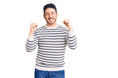 Gündelik kıyafetler giyen genç İspanyol adam başarı için heyecanlı kolları havada ve gözleri kapalı zaferi kutlarken gülümsüyor. Kazanan konsept. 