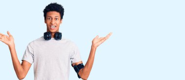 Spor kıyafetleri giyen ve kulaklık takan genç Afro-Amerikan adam zaferi mutlu bir gülümsemeyle kutluyor ve ellerini kaldırarak kazanan yüz ifadesi takınıyor. 