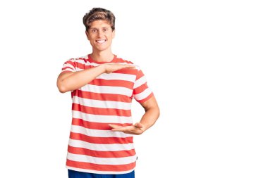 Elleriyle el kol hareketi yapan, büyük ve büyük beden işareti gösteren sıradan kıyafetler giyen genç yakışıklı bir adam. Kameraya bakıp gülümsüyor. ölçüm kavramı. 