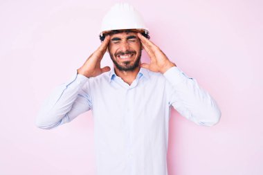 Kıvırcık saçlı yakışıklı genç adam ve ayı, mimar şapkası takıyor, başı ağrıyor çünkü stres altında. migren ağrısı. 