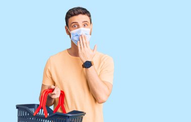 Alış veriş sepeti takan yakışıklı genç bir adam ve ağızlarını ağızla kapatan tıbbi bir maske, şok geçirmiş ve hata yapmaktan korkan. şaşırmış ifade 