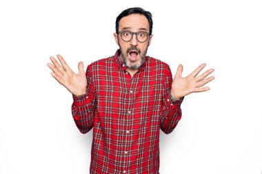 İzole edilmiş beyaz arka plan üzerinde gündelik gömlek ve gözlük takan orta yaşlı yakışıklı bir adam. Kolları açık, hiçbir fikri yok ve şüpheli bir yüzü var..