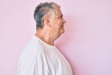 Beyaz tişört giyen, rahat bir görünüm takınan, kendine güveni olan yaşlı, gri saçlı bir adam.. 