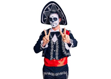 Arka planda ölü kostümü giymiş genç bir adam gülümseyerek kameraya bakıp zafer işareti yapıyor. İki numara.. 