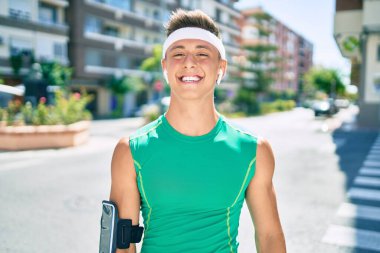 Genç İspanyol sporcu akıllı telefon ve kulaklık kullanıyor şehrin caddesinde yürüyor.