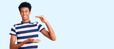 Genç Afrikalı Amerikalı sıradan kıyafetler giyen, elleri büyük ve büyük boy işareti gösteren, ölçü sembolü olan bir adam. Kameraya bakıp gülümsüyor. ölçüm kavramı. 