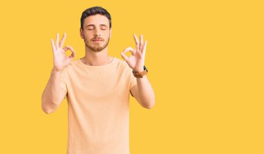 Ayılı yakışıklı genç adam gündelik sarı tişört giyiyor rahatla ve gözleri kapalı gülümse parmaklarıyla meditasyon hareketi yapıyor. yoga konsepti. 