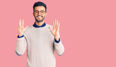 Zarif kıyafetler ve gözlük takan yakışıklı İspanyol adam dokuz numaralı parmaklarını gösterip gösterirken kendine güvenen ve mutlu bir şekilde gülümsüyor.. 