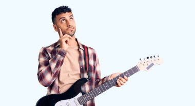 Elektro gitar çalan genç bir İspanyol. Ciddi bir yüz ifadesi. Elleri çenesinde soru sormayı düşünüyor. 