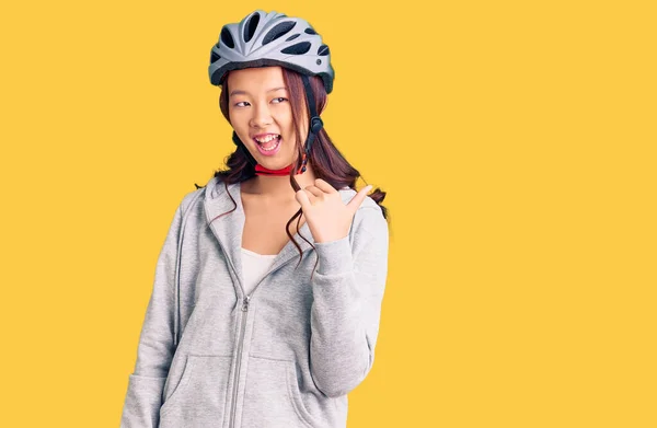 若いです美しいです中国の女の子身に着けています自転車ヘルメット笑顔で幸せな顔を見てと親指アップで側面を指して — ストック写真