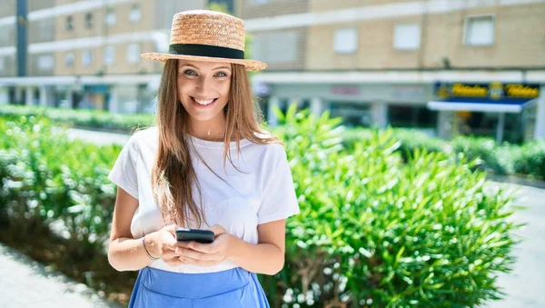 Genç sarışın kadın tatilde gülümsüyor. Şehrin caddesinde akıllı telefon kullanıyor.