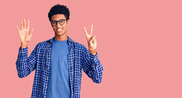 自信を持って幸せな笑みを浮かべている間 若いアフリカ系アメリカ人の男性は カジュアルな服や眼鏡を着て指の番号7で示すと指摘します — ストック写真