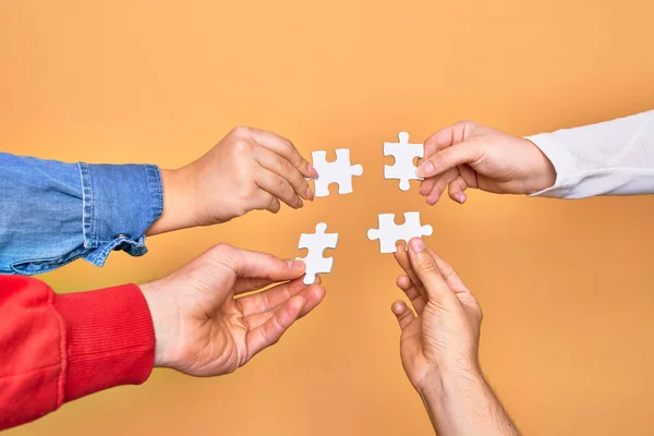 Hands of caucasian young people connecting pieces of puzzle over isolated yellow background