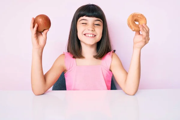 Niña Joven Con Bang Sosteniendo Manzana Roja Rosquilla Sentada Mesa — Foto de Stock