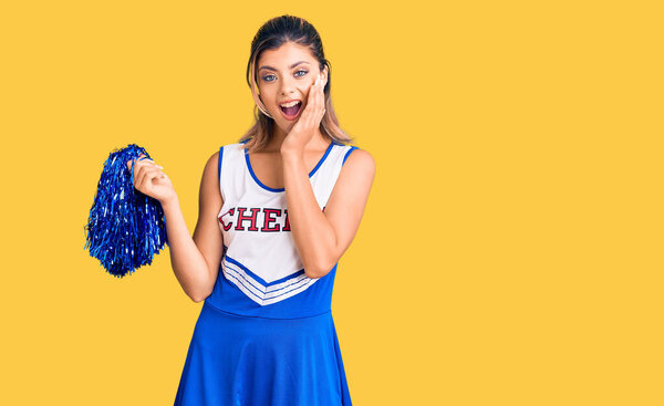 Young beautiful woman wearing cheerleader uniform afraid and shocked, surprise and amazed expression with hands on face 