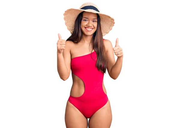 穿着泳衣 戴着夏帽的年轻美丽的拉丁女孩成功地做了一个积极的手势 竖起大拇指 微笑着 快乐地 快乐的表达和胜利的姿态 — 图库照片