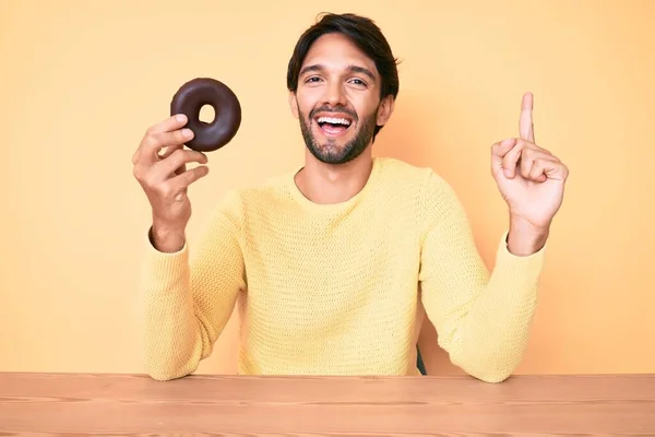 Όμορφος Ισπανός Που Κρατάει Ντόνατ Χαμογελώντας Μια Ιδέα Ερώτηση Δείχνοντας — Φωτογραφία Αρχείου