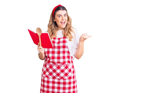 Joven Mujer Caucásica Usando Delantal Sosteniendo Libro Recetas Cuchara Sonriendo — Foto de Stock