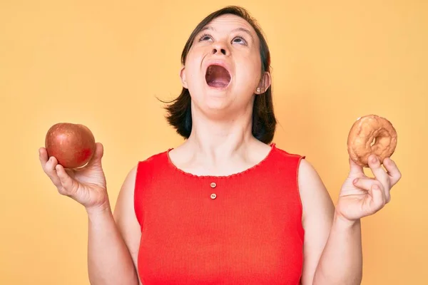 布鲁内特妇女与唐氏综合症持有红苹果和甜甜圈坐在愤怒和疯狂的尖叫沮丧和愤怒 怒气冲冲地大叫 — 图库照片