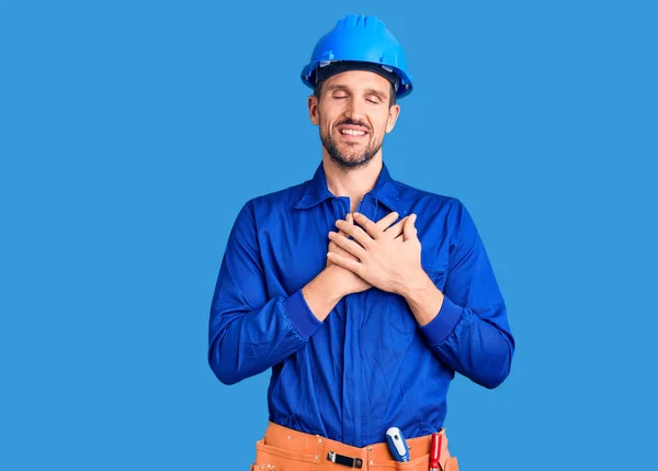 労働者の制服を着た若いハンサムな男と目を閉じて胸に手で笑みを浮かべて 顔に感謝のジェスチャー 健康の概念 — ストック写真