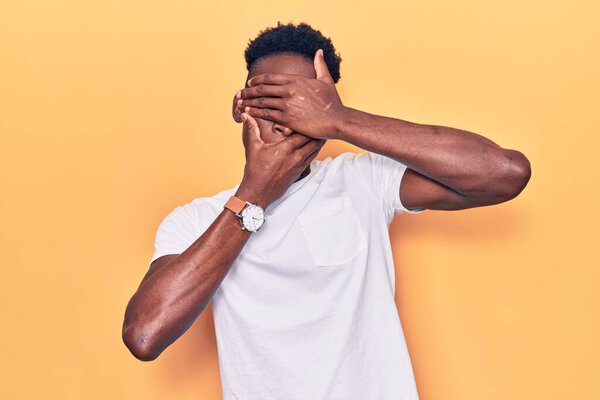 Young african american man wearing casual clothes covering eyes and mouth with hands, surprised and shocked. hiding emotion 