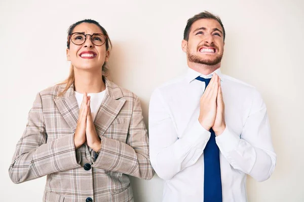 Beautiful couple wearing business clothes begging and praying with hands together with hope expression on face very emotional and worried. begging.