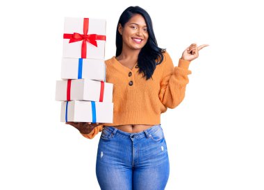 Uzun saçlı İspanyol kadın hediyeler tutuyor. Gülümsüyor, mutlu bir şekilde elini ve parmağını yana doğru gösteriyor. 