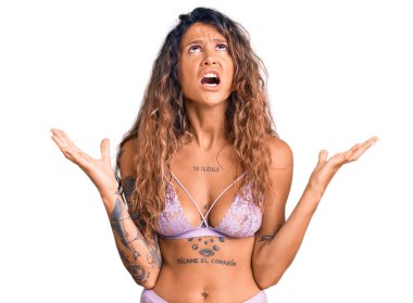 Dövmeli, deli gibi iç çamaşırı giyen, bağırıp çağıran saldırgan ifadeli ve kollarını kaldırmış genç İspanyol bir kadın. hüsran kavramı. 