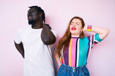 Irklar arası çift, gündelik kıyafetler giyip boyun ağrısı çekiyor. Boynuna elle dokunuyor. Kas ağrısı çekiyor. 