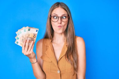 Avro banknotları tutan genç sarışın kız balık suratlı ve şaşı gözlü, çılgın ve komik.. 