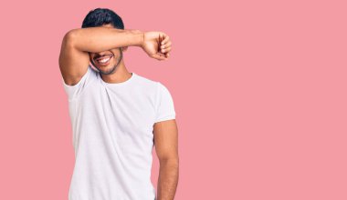 Genç latin adam günlük kıyafetler giyip kollarıyla gözlerini kapatıyor neşeli ve komik gülümsüyor. kör kavram. 