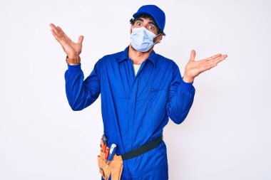 Kıvırcık saçlı ve ayılı yakışıklı, tamirci üniforması giyen ve güvenlik maskesi takan, kafası karışık, kolları açık, hiçbir fikri olmayan, şüpheli yüzlü bir genç.. 