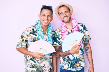 Yazlık tişört giyen, el ele tutuşan iki genç eşcinsel. Pozitif ve mutlu görünüyorlar. Dişlerini gösteren bir gülümsemeyle ayakta duruyorlar. 