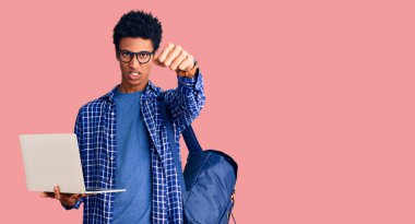 Genç Afro-Amerikalı bir adam sırt çantası tutuyor. Dizüstü bilgisayar kullanıyor. Öfkeyle bağırıyor, öfkeyle bağırıyor ve el kaldırıyor. 