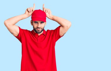 Sakallı, teslimat üniformalı, komik hareketler yapan genç yakışıklı bir adam. Parmağını boynuz gibi kafasının üstünde gezdiriyor. 