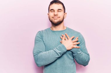 Elleri göğsünde gülümseyen sıradan bir süveter giyen genç yakışıklı bir adam. Minnettar bir yüz ifadesiyle gözleri kapalı. sağlık kavramı. 